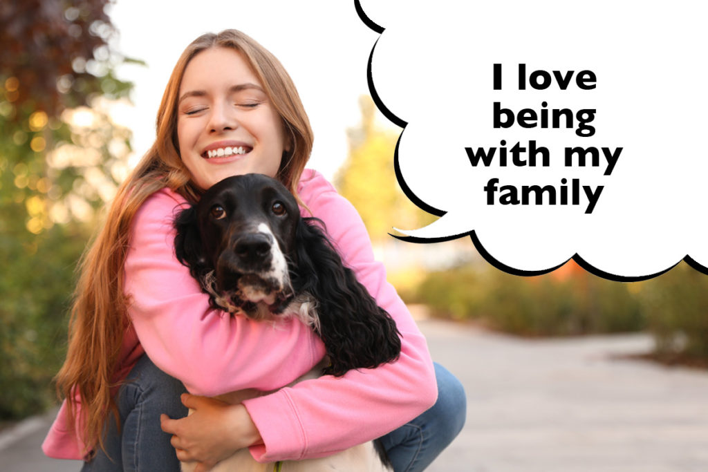 Teenager hugging her Springer Spaniel outside with a speech bubble that says 'I love being with my family'